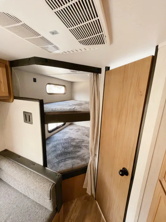 Inside an RV rental: view of the bunk beds with windows, a comfortable seating area, and a privacy curtain.. Cherokee MKSE22 2023