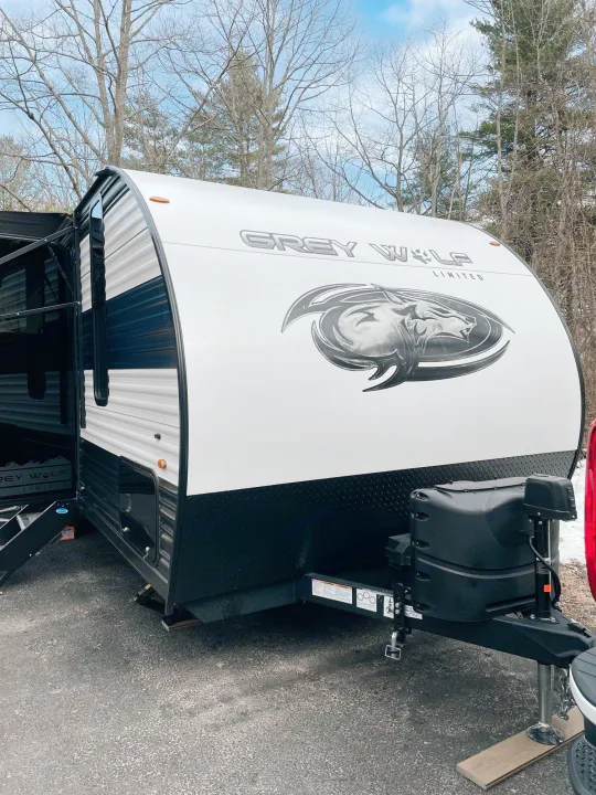 A white and black Grey Wolf travel trailer, ideal for your next RV rental, parked on asphalt with trees in the background.. Cherokee MKSE22 2023