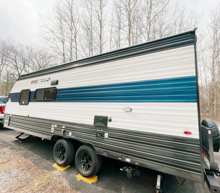 Grey Wolf travel trailer RV rental, white with blue stripes, set up for camping on yellow blocks under bare trees.. Cherokee MKSE22 2023