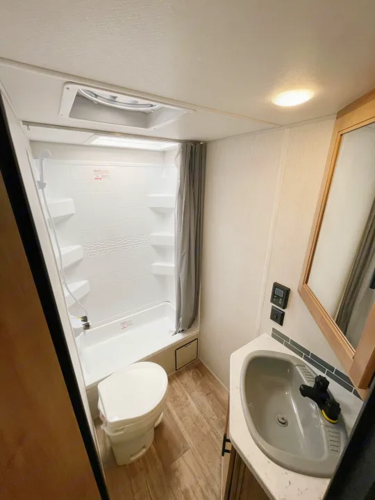 This bright RV rental bathroom features a compact shower, toilet, and sink vanity with a mirror and wood-look flooring.. Cherokee MKSE22 2023