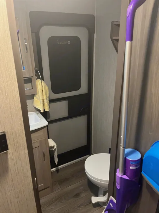 Compact RV rental bathroom with sink, toilet, door, and cleaning essentials.. Coachmen Freedom Express 2021
