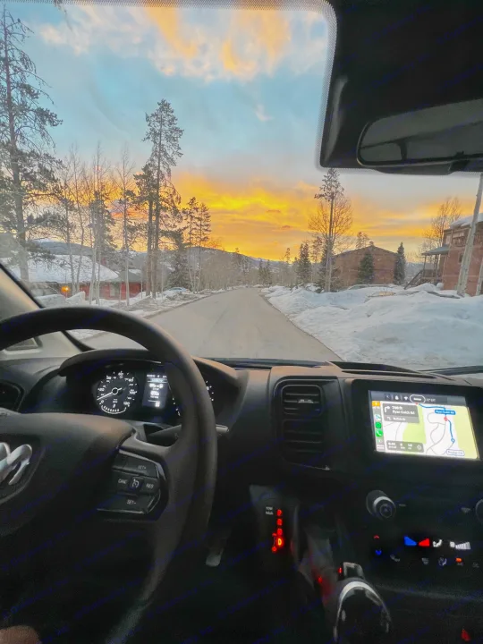 Driver's view from an RV rental at sunrise on a snowy mountain road. Dashboard, navigation to Ryan Gulch Rd, and vibrant sky.. Ram Promaster 2022