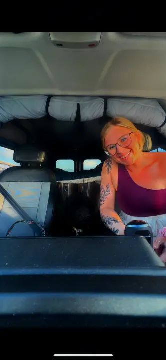 Smiling woman & black dog in their RV rental. Cozy camper van interior, perfect for pet-friendly adventures.. Ram Promaster 2022