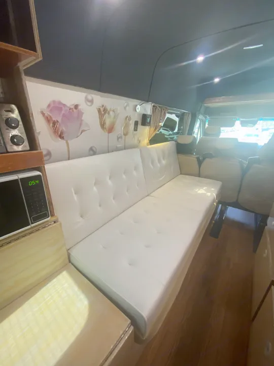 Inside this modern rv rental: a comfy white sofa bed, kitchenette with microwave (0:54), floral walls, & wood floor. Ready for travel!. Vanworks Mercedes Benz Sprinter 2021