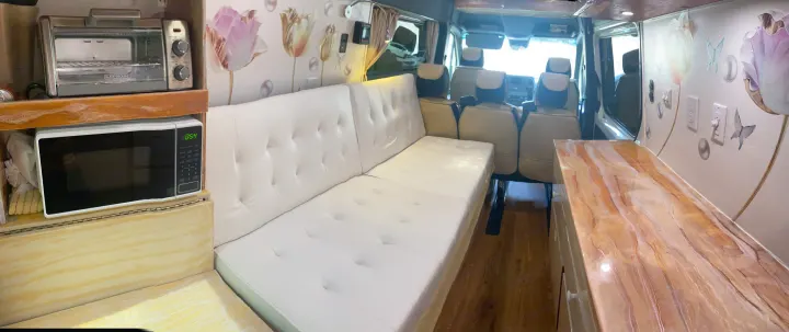 Spacious RV rental living area with white futon, microwave, toaster oven, and decorative counter. Ideal for travel!. Vanworks Mercedes Benz Sprinter 2021