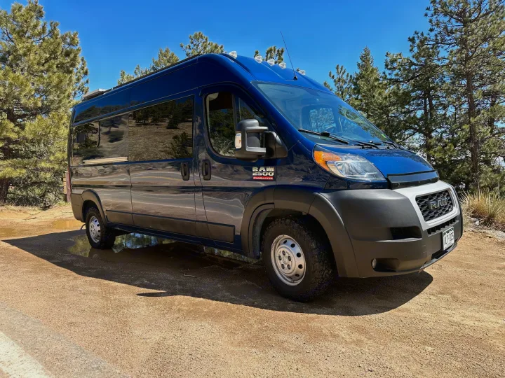 Blue Ram ProMaster RV rental van on a dirt road with puddles & pine trees under a clear sky. Your next adventure awaits!. Ram Promaster 2500 2021