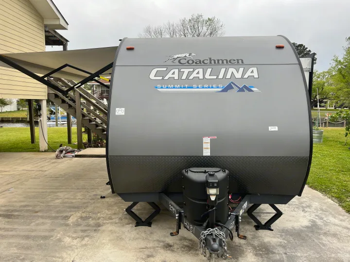 Grey Coachmen Catalina travel trailer, ideal for an RV rental, parked by a waterfront home with an extended awning.. Forest River Coachmen Catalina Summit 2022