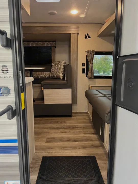 View from the open door of an RV rental showing the living space with a dinette, a bunk, and wood laminate flooring.. Forest River Coachmen Catalina Summit 2022