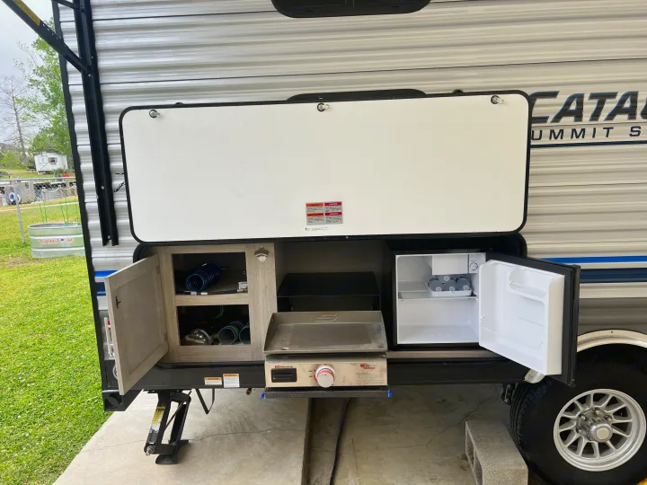 An RV rental's outdoor kitchen featuring a griddle, mini-fridge, and storage compartments ready for use.. Forest River Coachmen Catalina Summit 2022
