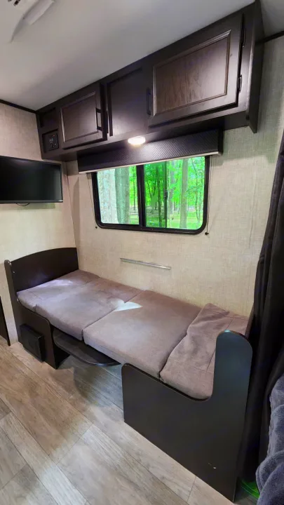 Cozy rv rental interior with a convertible sofa bed, overhead storage, and a TV. Enjoy the forest view from the window.. Jayco Jay Flight 2022