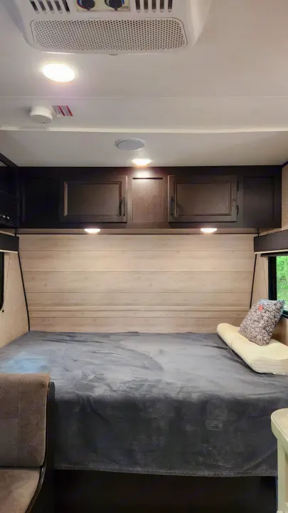 Cozy RV rental bedroom featuring a gray bed, light wood paneling, and overhead storage cabinets. Ideal for restful travels.. Jayco Jay Flight 2022
