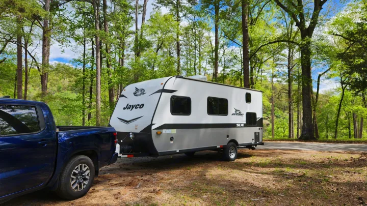 Scenic RV rental: A Jayco travel trailer hooked to a blue truck in a sunlit forest campsite.. Jayco Jay Flight 2022