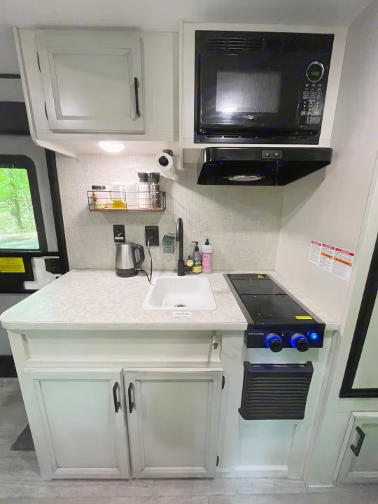 Well-equipped RV rental kitchen featuring a microwave, sink, kettle, and cooktop on a light countertop.. Jayco Jay Flight 2022