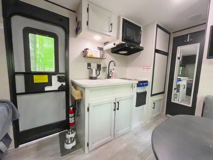 RV rental interior: modern kitchen, dining area, and bright exit door leading to nature. Pet bowls by the entrance.. Jayco Jay Flight 2022