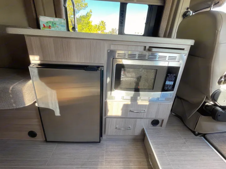 View inside an rv rental, highlighting the functional kitchenette with a microwave and stainless steel refrigerator.. Thor Sequence 2022