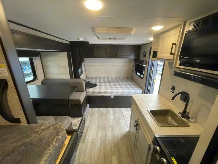 Interior of an RV rental showing a compact kitchen with sink/stove, a dinette, and a rear bedroom area.. Jayco Jay Flight SLX 2022