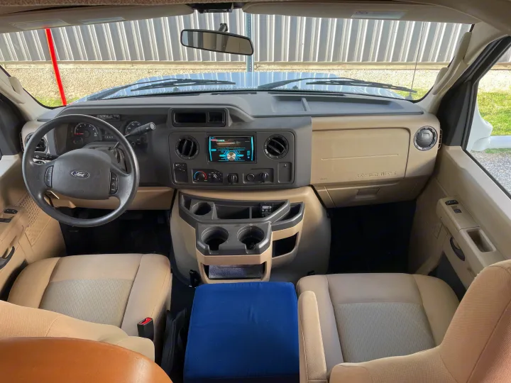 RV rental interior: A spacious van cockpit with a Ford steering wheel, tan seats, dashboard, and Pioneer stereo.. Thor Four Winds 2015