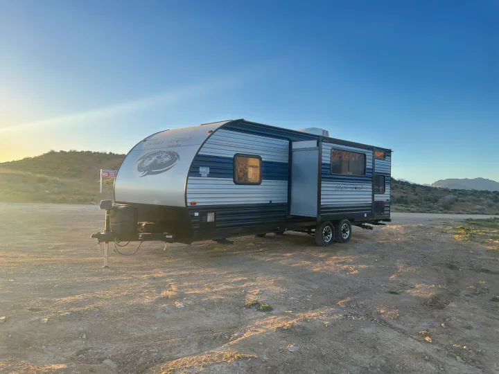 Grey Wolf travel trailer RV rental on a dirt lot in a vast desert landscape at sunset, ideal for camping.. Forest River Cherokee Grey Wolf 2022