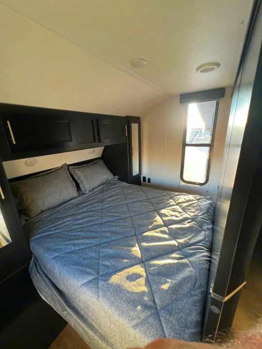 Comfortable RV rental bedroom with a bed, dark cabinets, and sunlit window. Your cozy sleeping area.. Forest River Cherokee Grey Wolf 2022