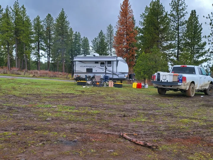 RV rental and pickup truck parked at a muddy campsite, surrounded by evergreen trees.. Jayco Jay Feather Micro 2022