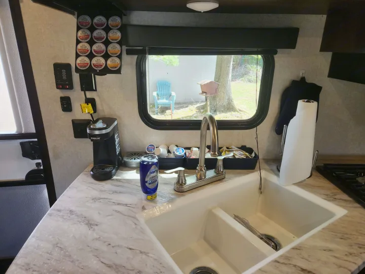RV rental kitchen counter with coffee maker, sink, coffee pods, RV controls, and a window looking out to a tree.. Jayco Jay Flight SLX 2019