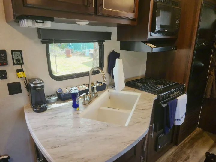 Compact RV rental kitchen with sink, stove, microwave, and coffee maker, showing practical use of space.. Jayco Jay Flight SLX 2019
