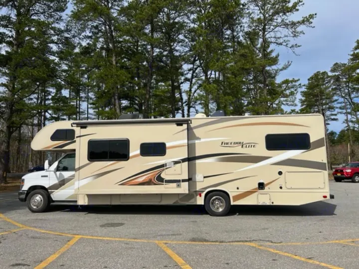 Spacious beige Freedom Elite Class C motorhome, ideal for an RV rental getaway. Parked among pine trees.. Thor Motor Coach Freedom Elite 2017