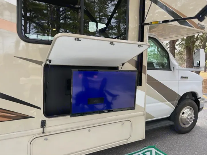 A beige RV rental features an open side compartment with a blue-screened outdoor TV, perfect for campsite entertainment.. Thor Motor Coach Freedom Elite 2017