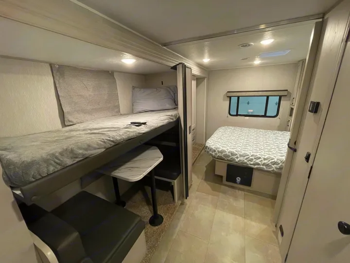 RV rental interior: Bunk beds and a dinette on the left, master bed with window on the right. Compact and functional.. Coachmen Freelander 2024
