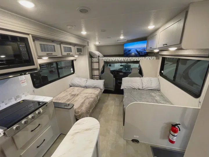 Modern RV rental interior with kitchen, two lower beds, overhead bunk, and entertainment TV. Bright and functional space.. Coachmen Freelander 2024