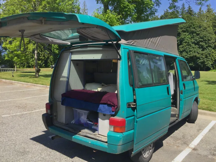 A teal camper van with an extended pop-top and open rear, revealing a bed & storage. Perfect for an rv rental trip.. Volkswagen T4 Westfalia Coach 1992