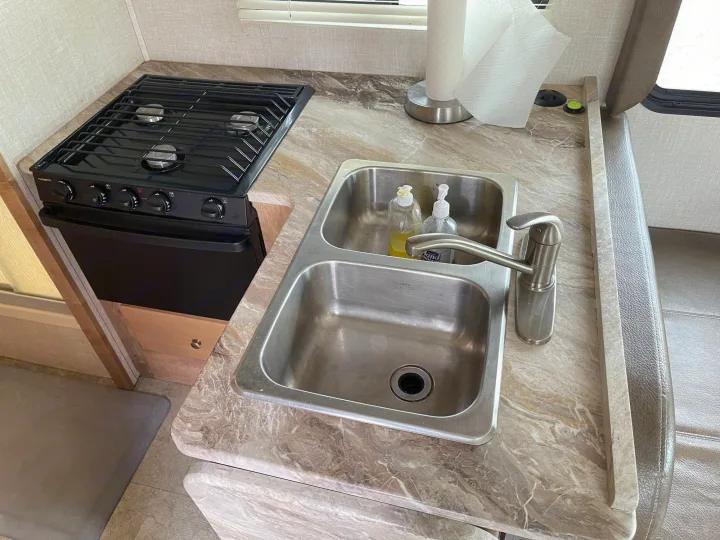 Tour this RV rental's kitchen: a 3-burner stovetop, double sink, and marbled counter with paper towels and soap.. Coachmen Leprechaun 2020