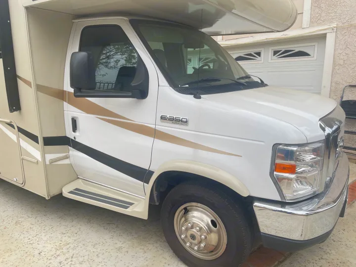 White and beige Ford E-350 Super Duty motorhome RV rental parked in a driveway.. Coachmen Leprechaun 2020