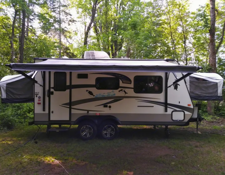 RV rental: A modern hybrid travel trailer with an extended awning is parked at a forested campsite, ready for adventure.. Other Other 2015