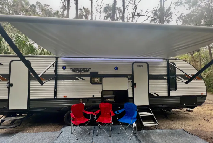 Relaxing at the campsite! This RV rental features an awning, outdoor kitchen, and comfy chairs. Perfect camping setup.. Forest River Wildwood X-Lite 2022