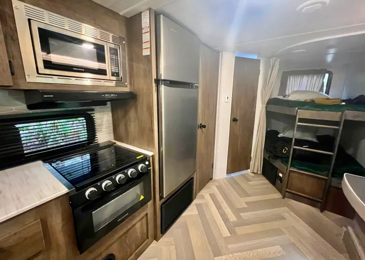 RV rental interior: compact kitchen (microwave, stove, fridge) and bunk beds, showing efficient living space.. Forest River Wildwood X-Lite 2022