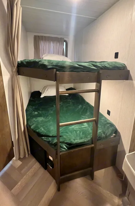 Cozy bunk beds with green blankets and pillows inside an RV rental, offering compact sleeping space.. Forest River Wildwood X-Lite 2022