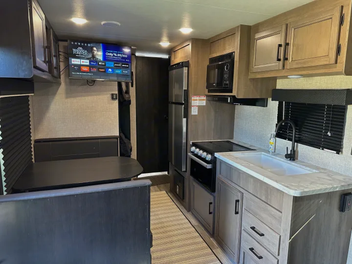 Modern RV rental interior featuring a full kitchen with appliances, dining booth, and TV displaying streaming services.. Jayco Jay Flight SLX 2022
