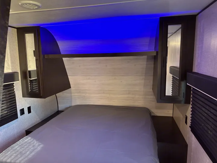 RV rental bedroom: a modern interior with a comfy bed, blue LED lighting, overhead storage, and convenient bedside outlets.. Jayco Jay Flight SLX 2022