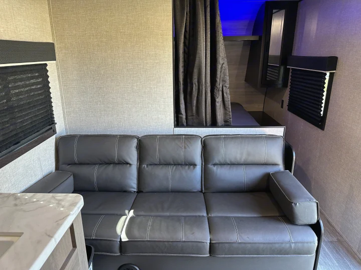 Modern RV rental living space featuring a dark gray sofa, bunks with blue light, and privacy blinds.. Jayco Jay Flight SLX 2022