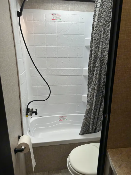 Inside a clean RV rental, this bathroom features a white tub/shower with a patterned curtain, toilet, and toilet paper holder.. Jayco Jay Flight SLX 2022