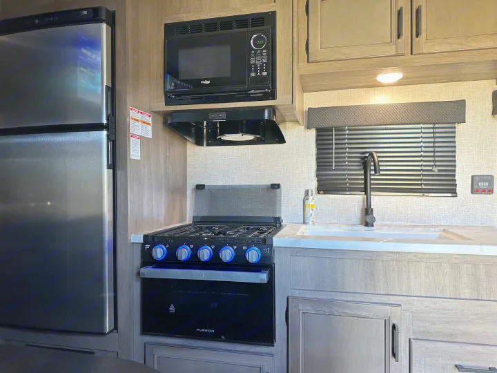 Tour a sleek RV rental kitchen! Features include a stainless steel fridge, microwave, gas stove with blue lights, and sink.. Jayco Jay Flight SLX 2022
