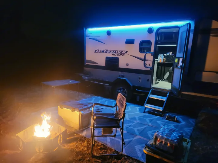 Jay Feather Micro RV rental setup at night, with bright blue awning lights, a glowing campfire, and cozy outdoor area.. Jayco Jay Feather Micro 2022