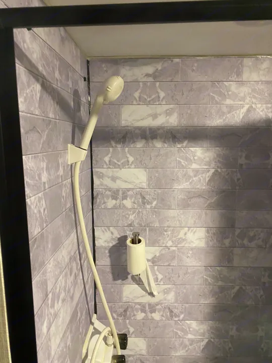 Compact RV rental shower with gray marble-look tiles, handheld showerhead, and toilet paper holder. Efficient design.. Braxton Creek Bushwhacker Plus 2022