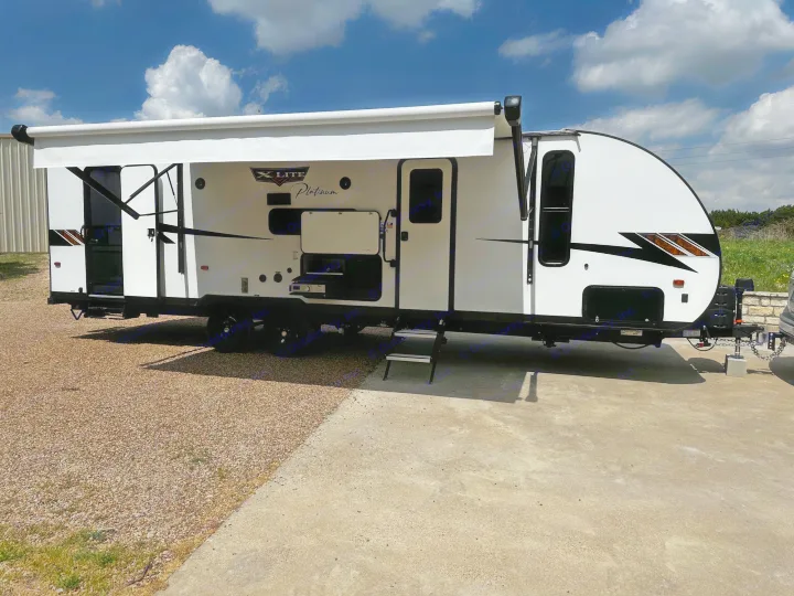 Clean white RV rental, awning out, parked on concrete/gravel. Ideal for outdoor recreation.. Forest River Wildwood X-Lite 2023