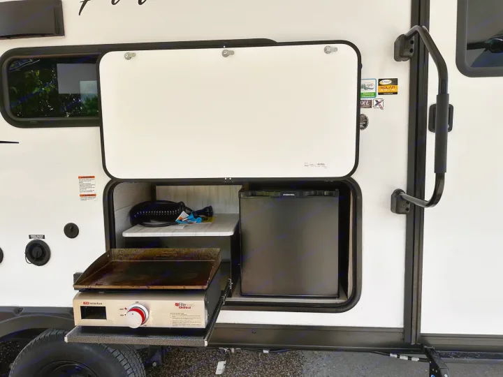 RV rental convenience: Outdoor kitchen with griddle & mini-fridge, perfect for camp meals.. Forest River Wildwood X-Lite 2023