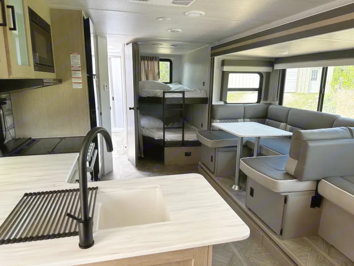 An RV rental's inviting interior, showing the kitchen, dining booth, and cozy bunk beds.. Forest River Wildwood X-Lite 2023