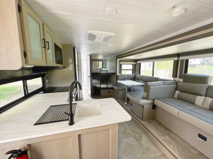 Inside a clean, modern RV rental: well-equipped kitchen, comfy living space, and bunk beds.. Forest River Wildwood X-Lite 2023