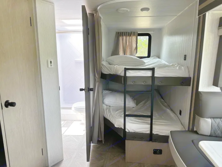 Experience RV rental comfort: twin bunk beds, a compact bathroom, and a dinette in a modern camper.. Forest River Wildwood X-Lite 2023
