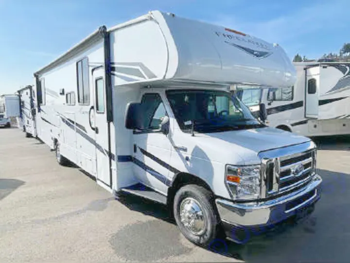 White Class C RV rental parked on a lot, ready for travel. Its truck-like front and cab-over bunk are visible.. Coachmen Freelander 2022